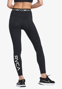 Leggings neri in tessuto elasticizzato, con vita alta, dotati di un cinturino grigio con logo e di un logo bianco RVCA stampato sulla gamba sinistra.