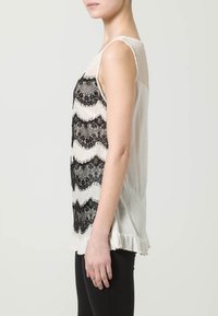 Mouwloze top met een crèmekleurige stofbasis en zwarte kantstrepen. Gerimpelde zoom en een gestructureerd achterpaneel voegen detail toe.