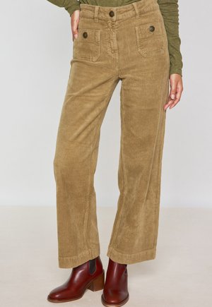 Pantalons à pattes larges en velours côtelé couleur brun clair avec poches avant et accents en boutons, associés à des bottines à talons brunes.