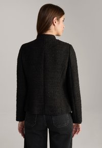 Zwart textuurjack met hoge kraag, voorzien van een getailleerde silhouette en lange mouwen. De achteraanzicht toont gestructureerde naden en subtiele patronen.
