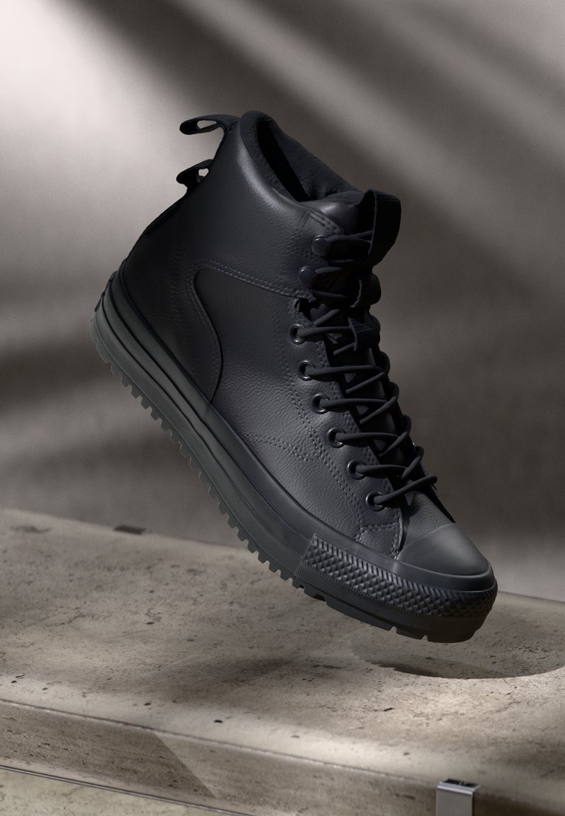 Zwarte hoge sneaker van leer met een gestructureerde afwerking, rubberen zool, ronde neuscap en een trekknoop aan de achterkant voor eenvoudig aantrekken.