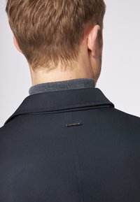 Giacca blu navy con colletto grigio testurizzato, caratterizzata da un'etichetta rettangolare sul retro e un design su misura.