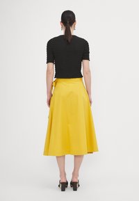 Top nero, testurizzato, a maniche corte abbinato a una gonna gialla a vita alta, lunga fino al ginocchio. Sandali neri con tacco completano l'outfit.