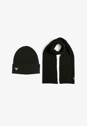Bonnet noir en tricot avec une texture côtelée et un petit détail en forme de cœur, associé à une écharpe côtelée assortie. Les deux sont de couleur noire.