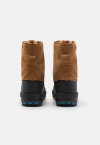 Ruskeat mokkakengät ja mustat kumisaappaat, jotka ovat matalat, tekstuuripintaiset ja sinisillä kumipohjilla. Ne sisältävät ompeleita ja vetoluukun.