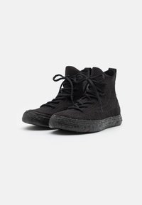 Zwarte high-top sneakers met een gestructureerde gebreide bovenkant, ronde neus en zwarte rubberen zool met gekleurde spikkels. Veters aan de voorkant voor sluiting.