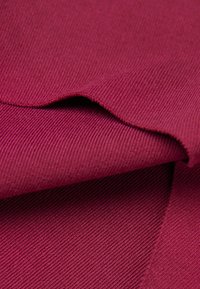 Burgundy ribbat tyg med en mjuk textur, visar en vikning på kanten och en subtil glans. Vävmönstret är fint och enhetligt.