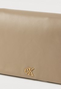 Μπεζ δερμάτινο πορτοφόλι με λεία υφή, σχεδιασμό με κλείσιμο διπλώματος και χρυσό λογότυπο "CK" στην μπροστινή πλευρά.