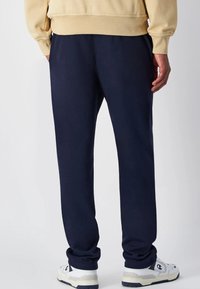 Navyblaue Sweatpants mit einer lässigen Passform, gefertigt aus weichem Stoff. Mit elastischem Bund und Bündchen. Kombiniert mit weißen Sportschuhen.