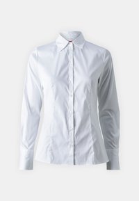 Chemise blanche cintrée à manches longues avec boutons et col pointu sur fond uni.