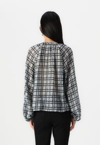 Blusa a quadri trasparente con design grigio chiaro e nero, schiena arricciata e maniche lunghe con polsini elastici.