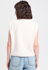 Haut sans manches de couleur crème en polaire texturée, avec une coupe décontractée et un ourlet arrondi, associé à un jean en denim bleu clair.