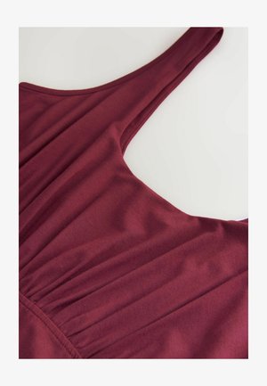 Burgundy sleeveless top with a smooth, stretchy fabric. Gathered detailing near the neckline and a subtle sheen on the material.