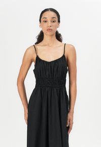 Abito nero senza maniche con corpino arricciato e vita elastica, gonna fluida, texture liscia e design minimale.
