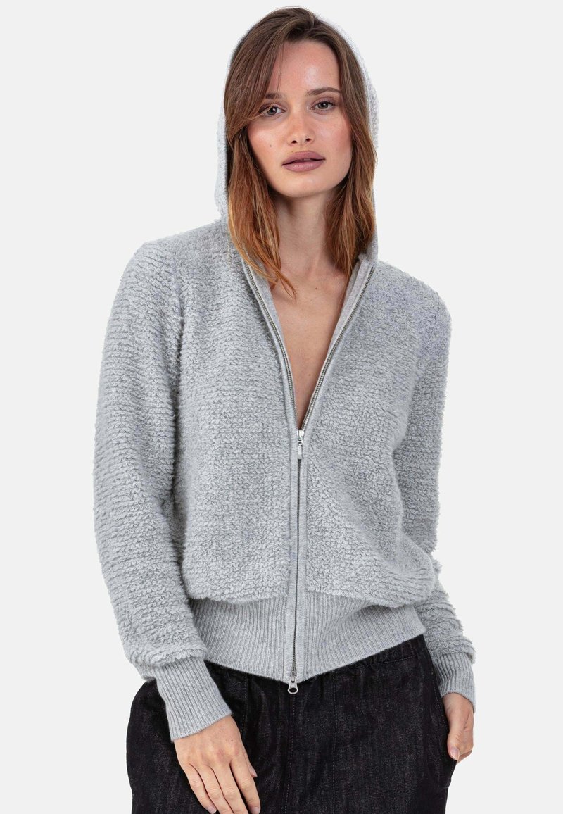 Sweat à capuche zippé gris clair avec une surface texturée, des poignets et un ourlet côtelés. Comprend une capuche et une silhouette ajustée. Tissu doux et duveteux.