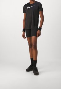 Camiseta deportiva negra de Nike con un logo blanco, combinada con pantalones cortos de compresión negros, calcetines negros y zapatillas de entrenamiento negras.