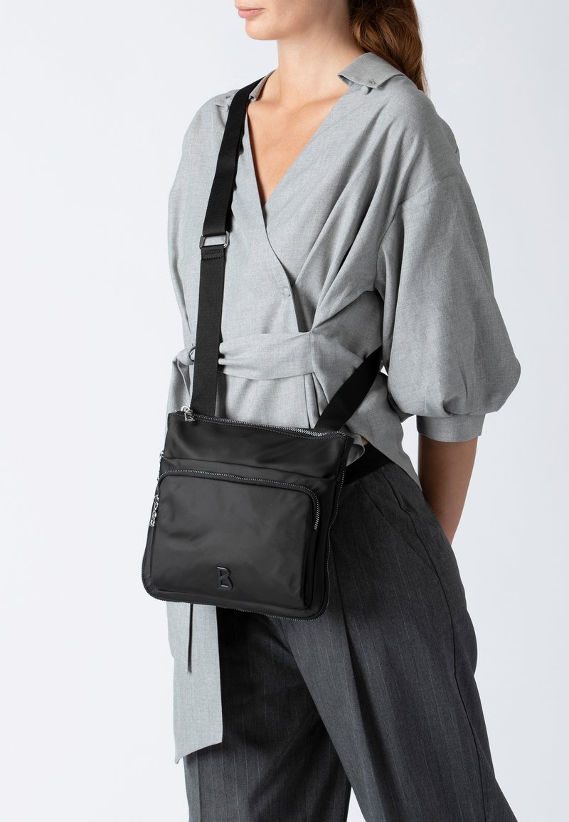 Borsa a tracolla nera realizzata in tessuto liscio, con chiusura con zip, tasca esterna e dettagli con logo sulla parte anteriore.