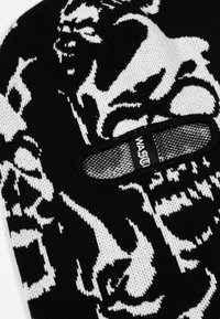 Crna pletiva kapa s bijelim grafičkim dizajnom i odvažnim uzorcima. Uključuje mali izrez sa teksturiranom trakom označenom "MAST."