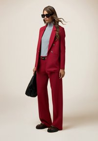 Rode op maat gemaakte blazer en brede broek, grijze coltrui, zwarte riem, oversized zwarte zonnebril en gestructureerde zwarte handtas.