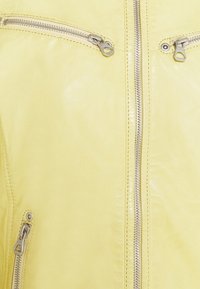 Giacca di pelle gialla con cerniere argentate, dotata di due tasche sul petto e una cerniera frontale. Tessuto liscio e vestibilità su misura.