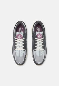 Nike Air sneakers hebben een combinatie van een grijs en lichtblauw mesh bovenwerk, met witte veters, een gevoerde kraag en een paarse binnenzool. Kenmerkende perforaties zijn aanwezig.