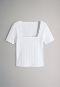 Top bianco a coste con maniche corte e ampio scollo quadrato, disteso su uno sfondo grigio chiaro.