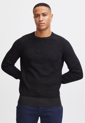 Svart strikket genser med ribbestruktur, rund hals, og kontrastkant. Lange ermer med en tettsittende design. Brun merkelappdetalj i midjen.