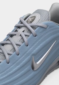 Ανοιχτό γαλάζιο αθλητικό παπούτσι Nike με γκρι κορδόνια και δίχτυ στη γλώσσα, που δείχνει το ασημί λογότυπο Nike swoosh σε επάνω μέρος από υφασμάτινη υφή.
