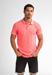 Rosa pikétröja med krage och korta ärmar, prydd med ett subtilt marinblått mönster. Matchad med svarta denimshorts.