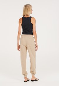 Helle beige Jogginghosen mit elastischen Bündchen, einem Kordelzugbund und zwei Gesäßtaschen. Kombiniert mit einem taillierten schwarzen Tanktop.