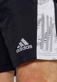 Shorts deportivos negros con un panel blanco que presenta un patrón de puntos y acentos grises, incluyendo el logo de Adidas y el diseño de las tres franjas.