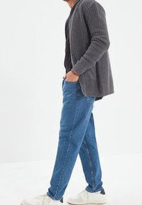 Cárdigan de punto gris, camiseta negra, jeans de pierna recta azules y zapatillas blancas con detalles en navy. El cárdigan presenta un tejido texturizado.