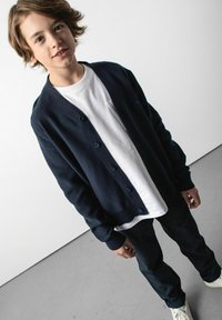 Granatowy kardigan z guzikami noszony na białej koszulce, zestawiony z ciemnymi dżinsami i białymi trampkami. Prosty design, miękka tekstura i swobodny krój.