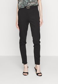 Svarta åtstramande byxor med en jämn textur, som har en subtil glans. Matchade med svarta sandaler med remmar och en mönstrad topp.