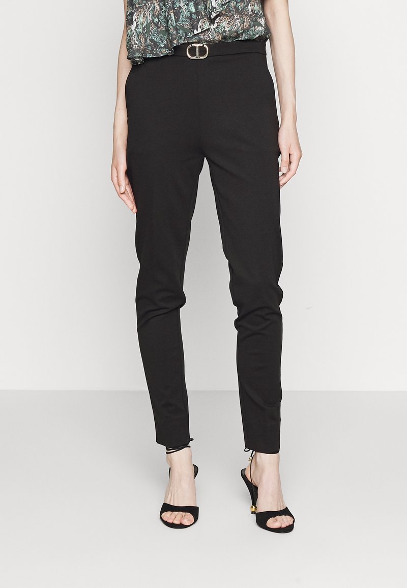 Svarta åtstramande byxor med en jämn textur, som har en subtil glans. Matchade med svarta sandaler med remmar och en mönstrad topp.