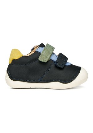 Zapatilla negra para niño pequeño con talón amarillo, lengüeta azul, correas de velcro verdes y negras, y suela blanca, mostrada de perfil sobre fondo blanco.