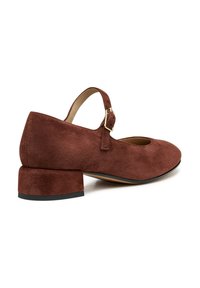 Chaussure en daim marron avec un bout arrondi et un petit talon bloc. Dispose d'une bride de cheville avec une boucle en métal. Doublure intérieure lisse.