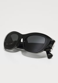 Schwarze Sonnenbrille mit großen, ovalen Gläsern, glänzendem Kunststoffrahmen und silbernen Hardwareakzenten. Verfügt über ein mutiges, modernes Design.