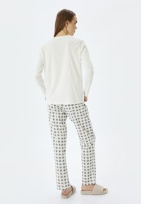 Camiseta blanca de manga larga combinada con pantalones de pijama de cuadros beige y gris, con un corte relajado y textura suave. Calzado de casa beige y acogedor.