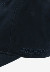 Czarna czapka z teksturowanej tkaniny, z zakrzywionym daszkiem i haftowanym logo "PROSTO" w kolorze dopasowanym do reszty na przednim panelu.