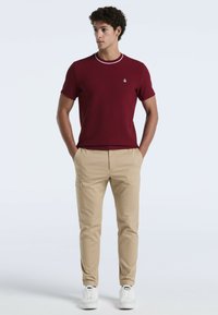 Bordeaux kortemouwen shirt met een contrasterende witte kraag, gecombineerd met kaki cargobroek en witte sneakers. Zachte textuur, casual pasvorm.