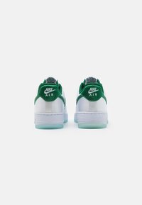 White Nike Air sneakers with green accents. Features a textured fabric on the back and a translucent rubber sole. Minimalistic design.