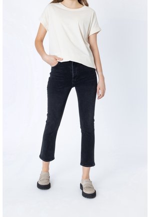 Beige puuvillane t-särk keeratud varrukatega, millele on sobitatud mustad lühikesed teksad kulunud äärega ja hallid libisevad kingad frillide detailiga.