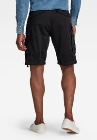 Svarta cargo-shorts med en avslappnad passform, med sidofickor och dragsko i nederkant. Tillsammans med en denimskjorta och vita sneakers.