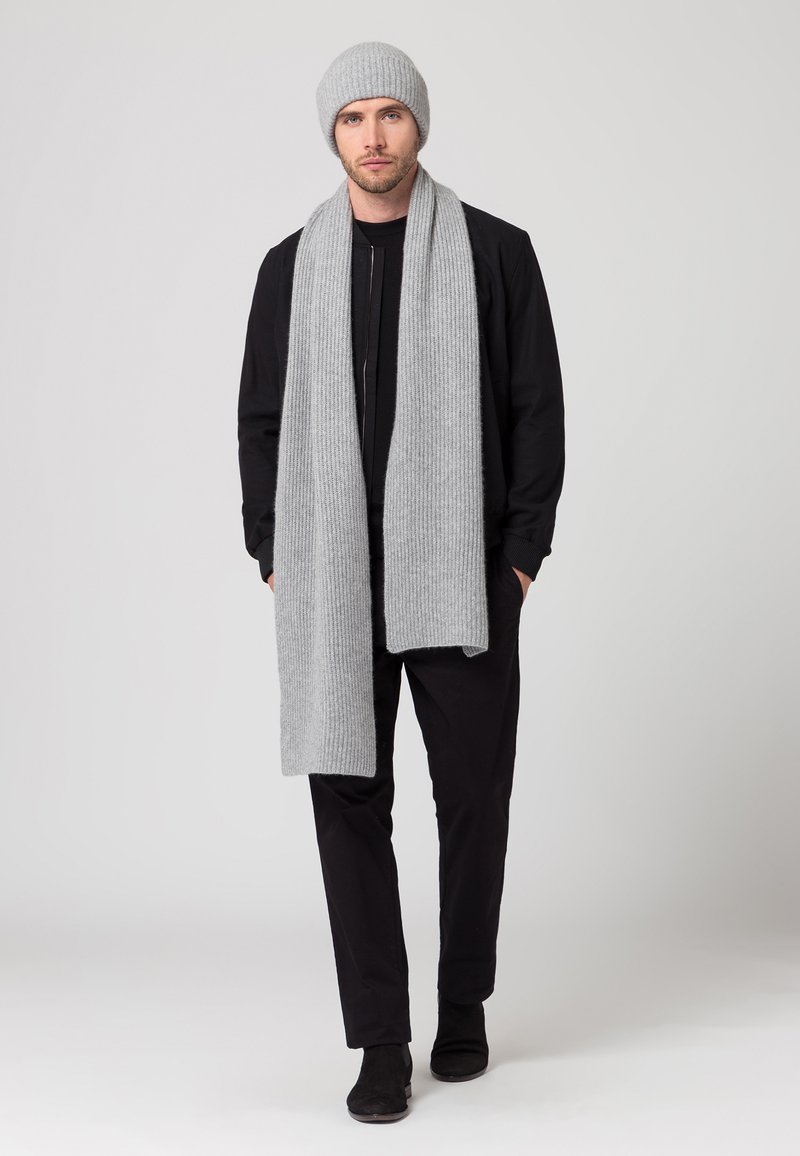 Berretto a coste grigio e sciarpa coordinata indossati con un outfit nero; la sciarpa è lunga e presenta una texture morbida.