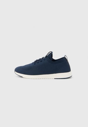 Navy blue knit sneaker with white sole, lace-up design, and pull tab on heel, shown in side profile on a plain light background.