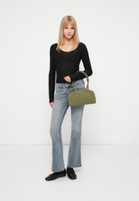 Sac à main en daim vert avec deux poignées courtes, de forme rectangulaire et accents en métal argenté. Porté avec un haut noir, un jean clair évasé et des chaussures noires.