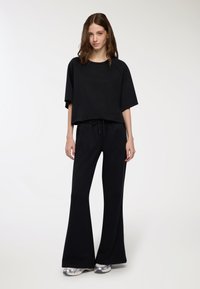 Maglietta nera corta con maniche corte abbinata a pantaloni neri a vita alta e a campana. Tessuto liscio, vita con cordino, dettagli metallici sulle scarpe.