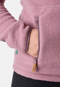 Fleecejack met een lichte roze kleur, voorzien van een ritszak en een zachte, gestructureerde oppervlakte. Inclusief een klein blauw en geel label op de mouw.