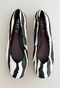 Ballerines à imprimé zèbre noir et blanc, fabriquées en matériau doux semblable à des poils, avec un bout arrondi et une semelle intérieure rembourrée pour plus de confort.